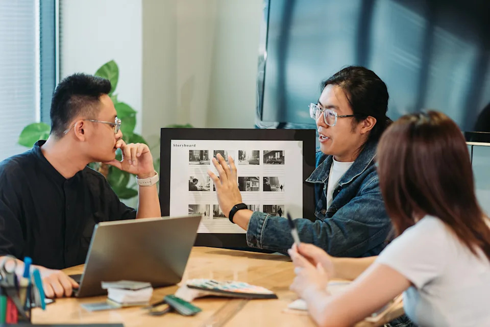 People in a meeting discussing images on a storyboard, seated around a table with a laptop and materials