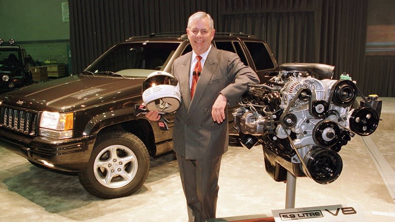 A Chrysler executive standing with a Jeep Cherokee and 5.9 liter engine