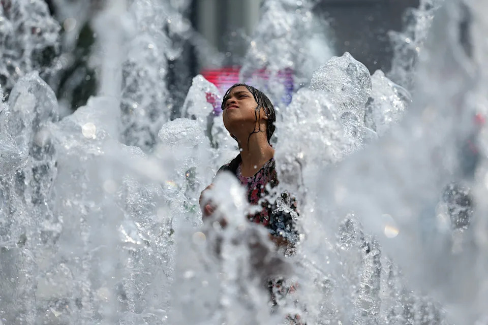 A child enjoys a public fountain on a hot day.