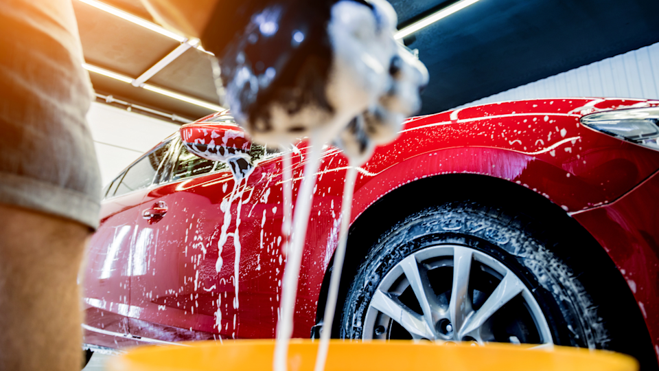 Worker washing red car with sponge on a car wash