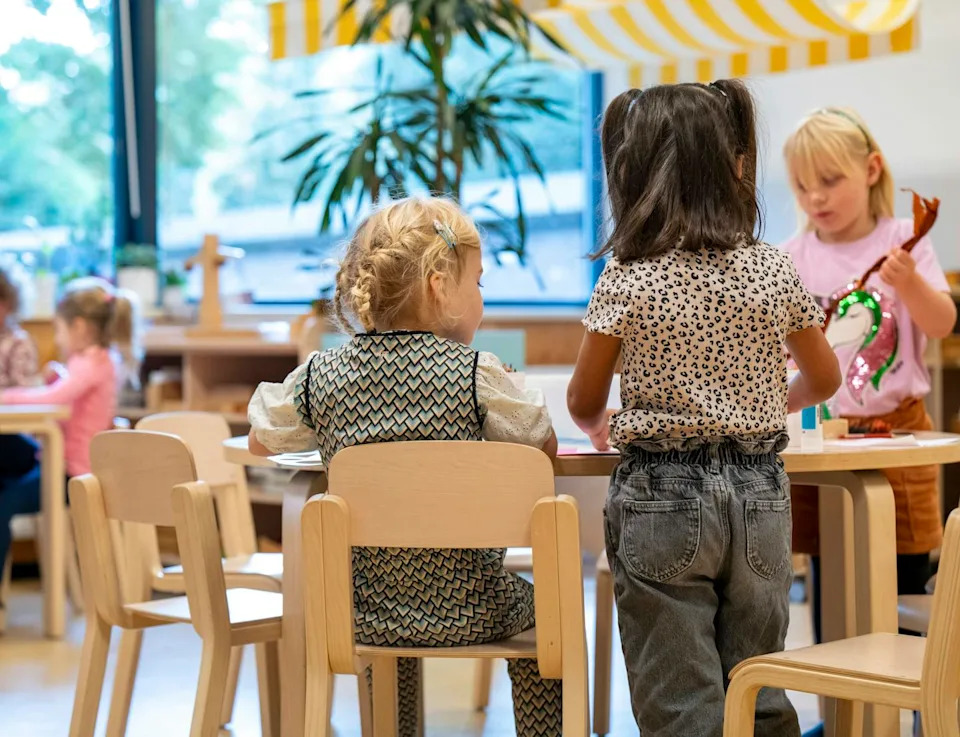 Toddlers engaged in an activity at a wooden table in a classroom.