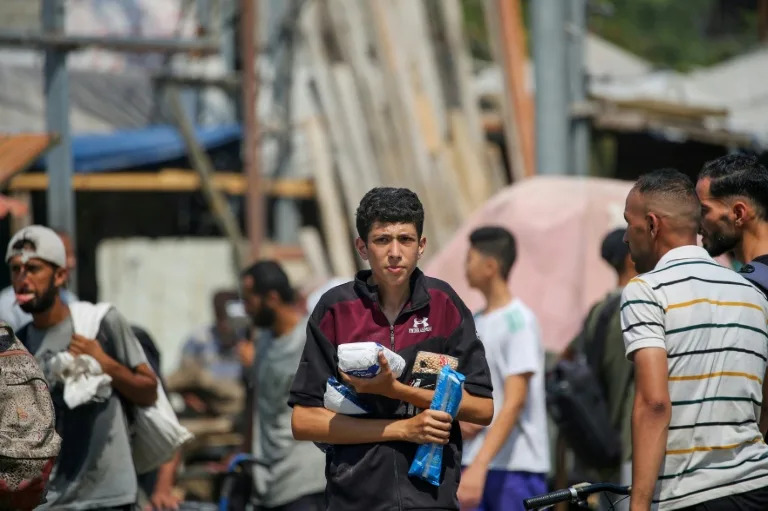 Palestinians return to Gaza's Nuseirat refugee camp with food they have managed to obtain from a distribution point in the Israeli-controlled Netzarim Corridor. (Eyad BABA)