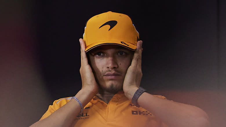 Lando Norris covers his ears during a press conference. Wearing McLaren orange.