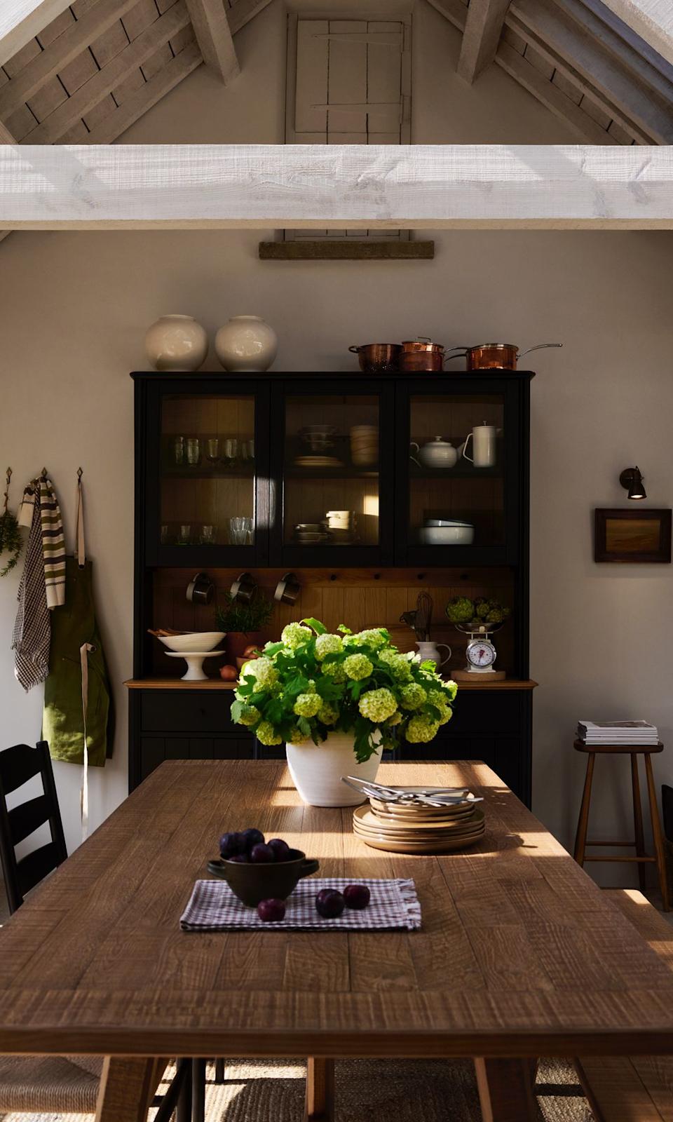 Cocina con alacena y mesa de madera con jarrón con flores, trapo de cocina de cuadros