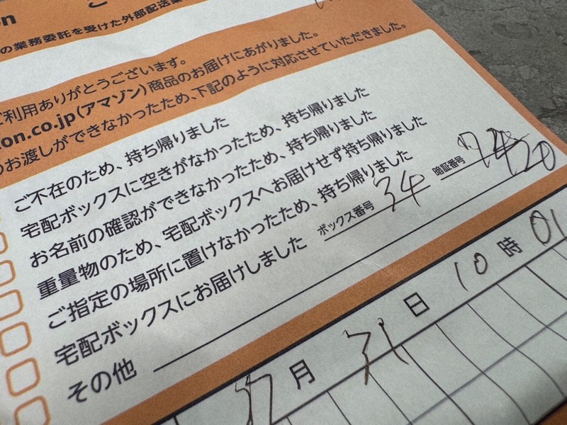 郵便受けに入っていたインターネット通販大手「アマゾンジャパン」の「ご不在連絡票」。記載された番号の宅配ボックスに暗証番号を入力すると鍵を開けられる。