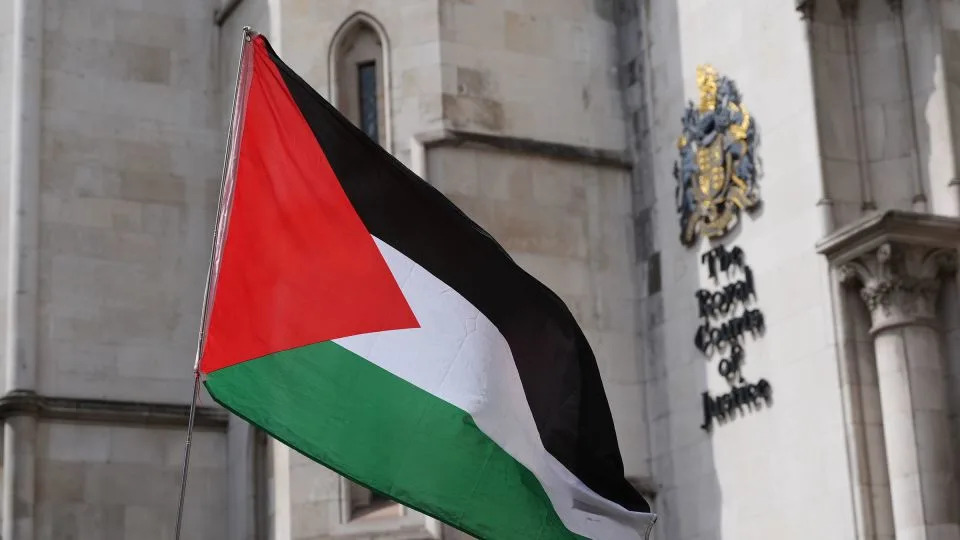 A Palestinian flag is waved outside The Royal Courts of Justice in central London on Wednesday. - Jonathan Brady/PA Images/Getty Images