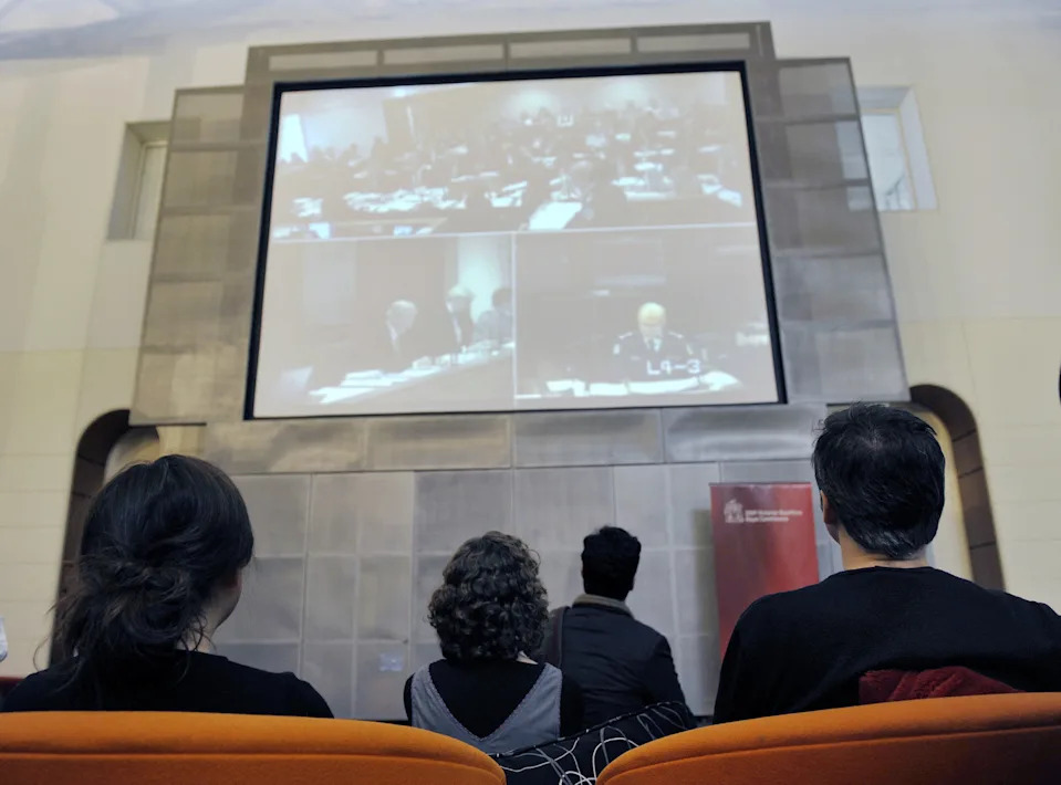 people watch a screen of hearings in a library