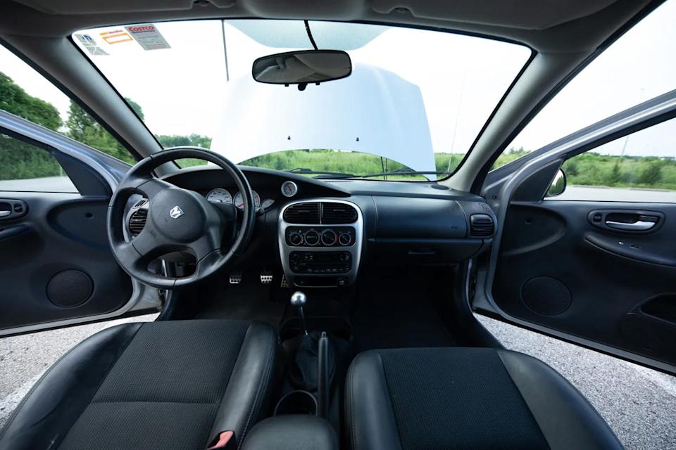 front interior view of sedan showing steering wheel, dashboard, open doors, and hood.