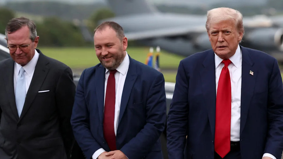 Three men from left to right - Warren Stephens, US Ambassador to the UK, Scottish Secretary Ian Murray and US President Donald Trump. They are at an airport with what is likely Air Force One blurry in the background. All three are wearing suits.