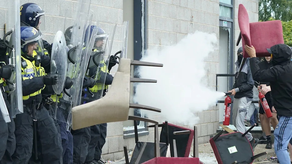 Protesters use fire extinguishers to attack officers. Chairs are thrown at the line of police officers who are holding up riot shields.