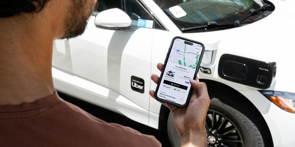 user checking uber app on smartphone in front of a white uber vehicle