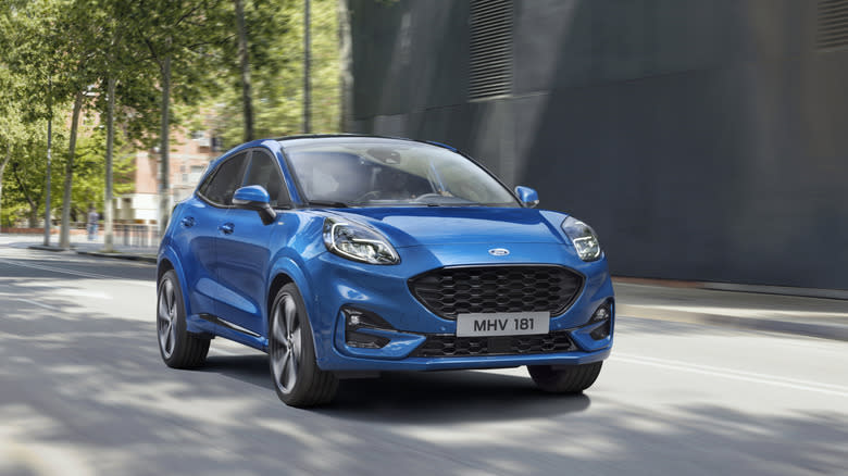 A blue Ford Puma driving down a city street