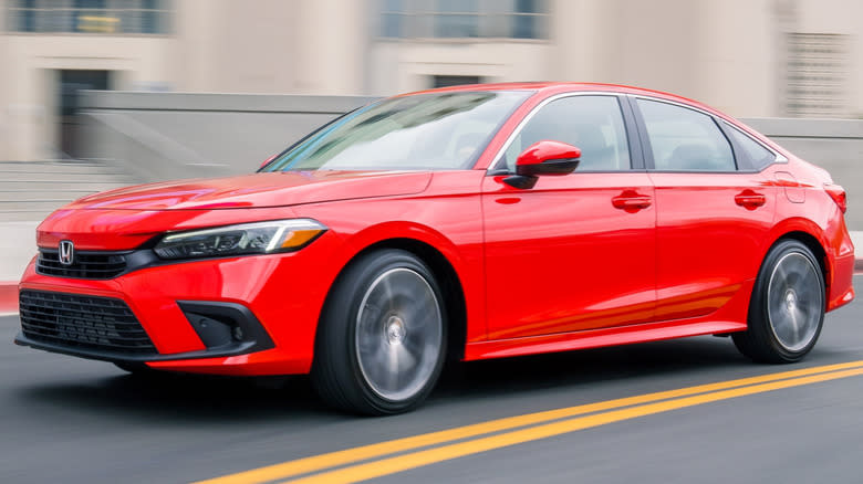 A red 2023 Honda Civic Sedan driving on a road with buildings in the background