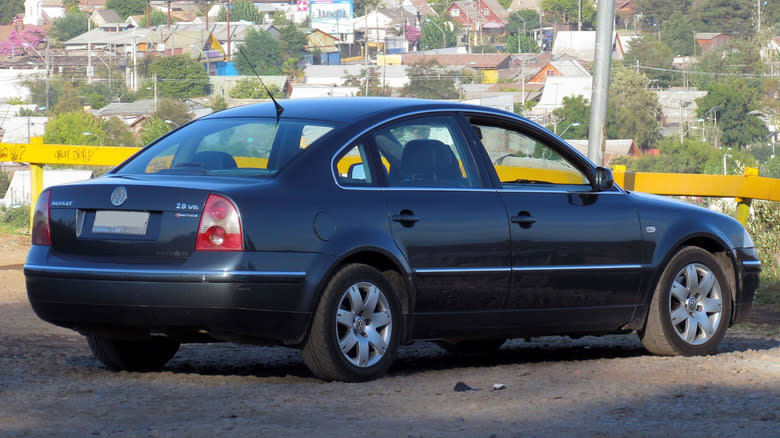 Rear three-quarters shot of a  dark gray Volkswagen Passat in front of homes