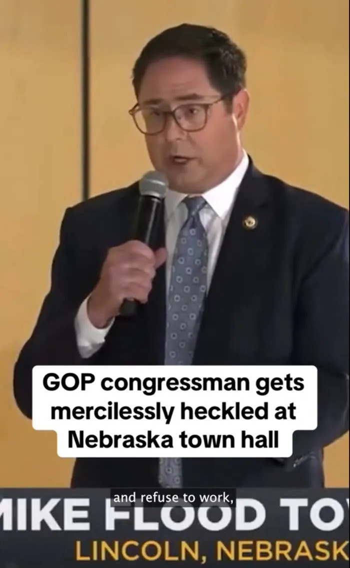 A man speaks at a town hall event in Nebraska. Text overlay: "GOP congressman gets mercilessly heckled at Nebraska town hall."
