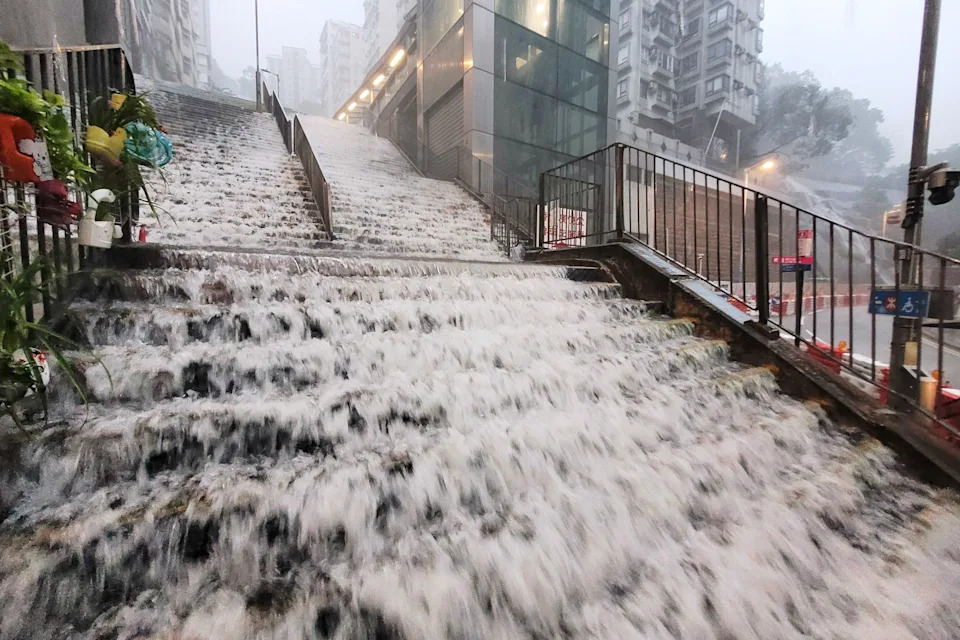 Floodwater flows down a wide public staircase during a rain storm.