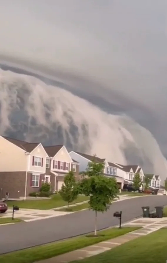 Massive wave-like cloud formation looms over suburban houses on a calm street, creating a dramatic natural scene