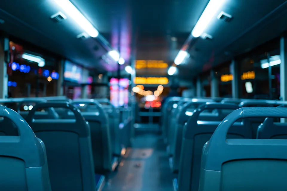 Empty bus interior at night, with rows of unoccupied seats and illuminated displays, suggesting off-peak or end-of-service hours