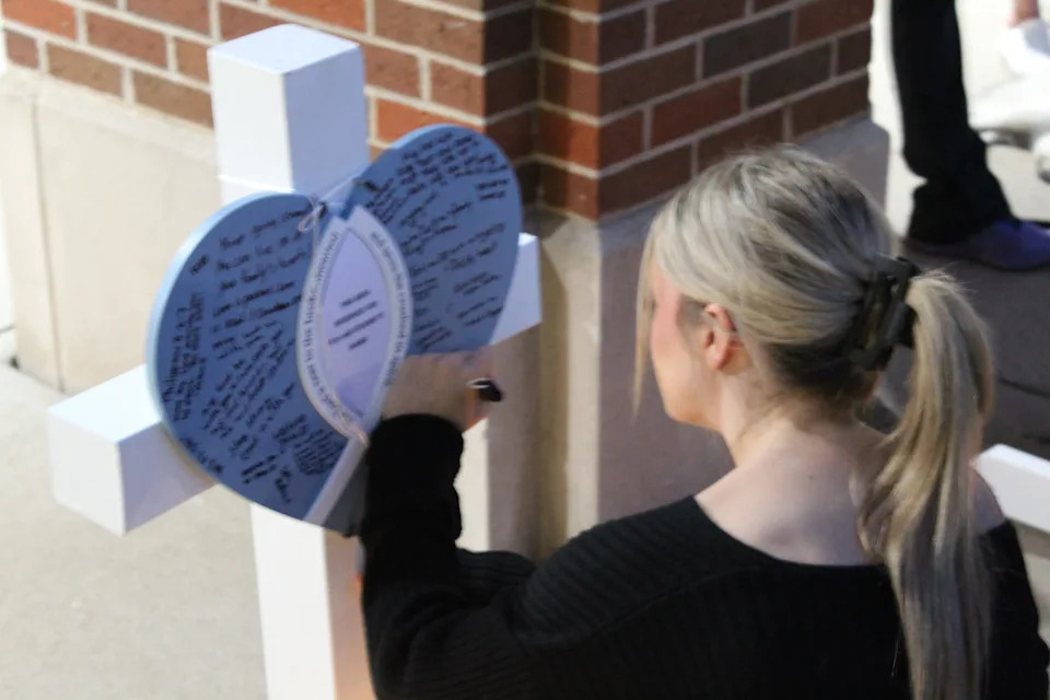 Vigil attendee Elaina Polding, 17, writing on a memorial cross for an eight-year-old child who died Aug. 27 during the Annunciation Church shooting in Minneapolis.