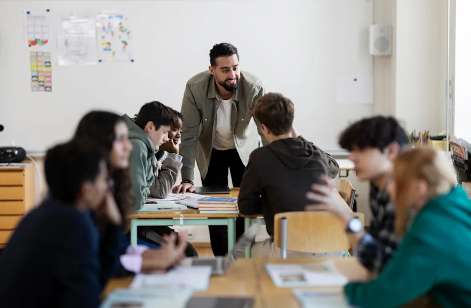 Teacher engages with students sitting at desks in a classroom, promoting discussion and collaboration