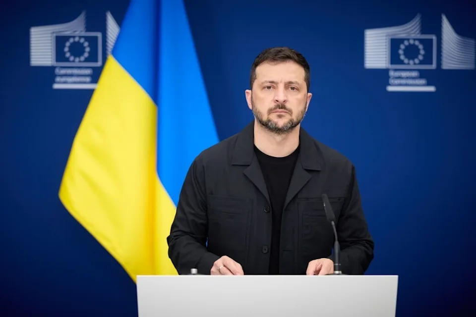 Person giving a speech at a podium, standing before EU and Ukrainian flags