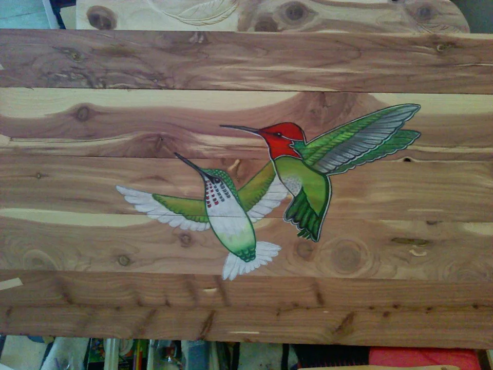 Two hummingbirds drawn on a piece of wood.
