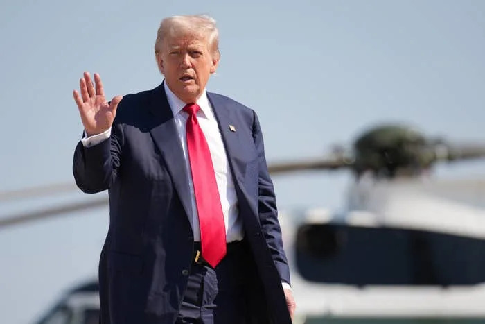 A man in a suit and red tie waves while standing in front of a helicopter
