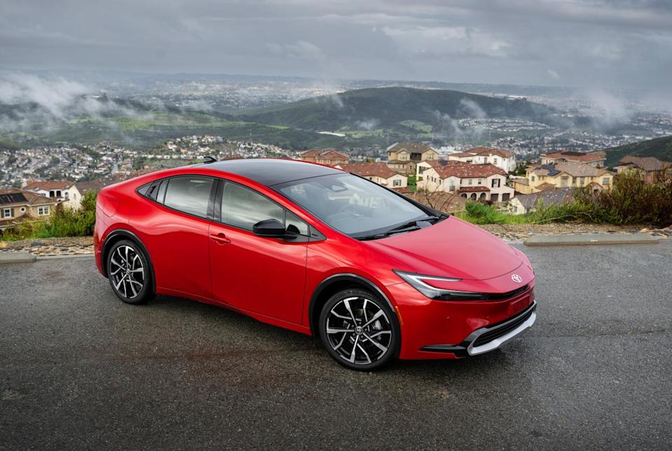 A bright red car parked on a road overlooking homes and hills